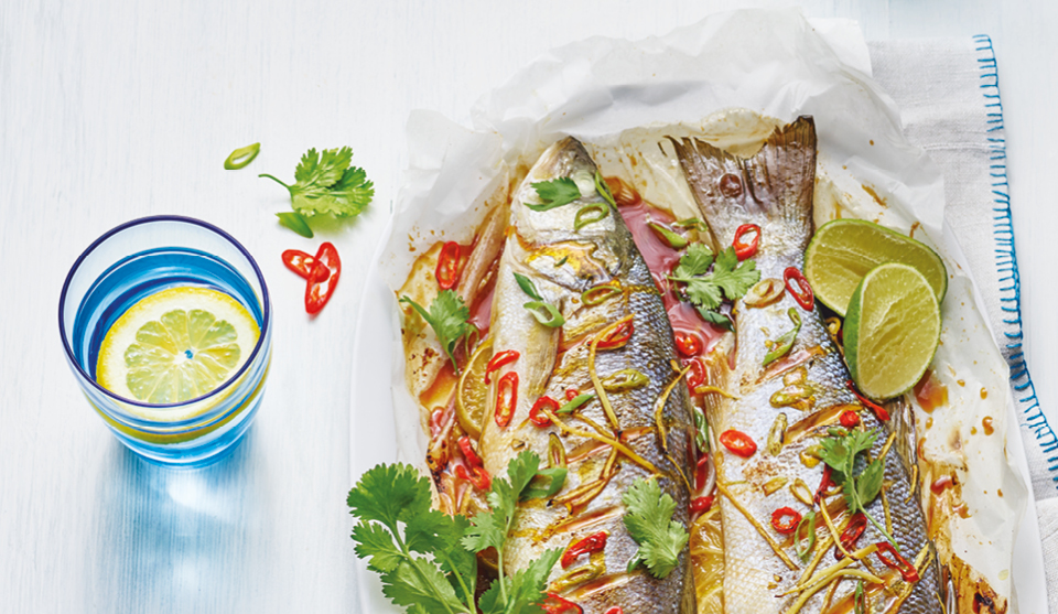 Asian Style Grilled Fish served on baking paper topped with coriander and lime wedges