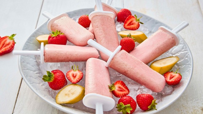 Banana and Strawberry Milk Pops displayed in a large bowl, on top of ice and surrounded by sliced strawberries and bananas