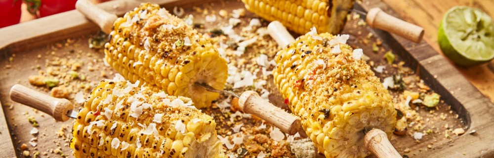 BBQ Sweetcorn with Chilli Butter, served on corn holders, on a wooden board