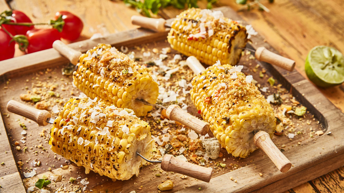 BBQ Sweetcorn with Chilli Butter, served on corn holders, on a wooden board