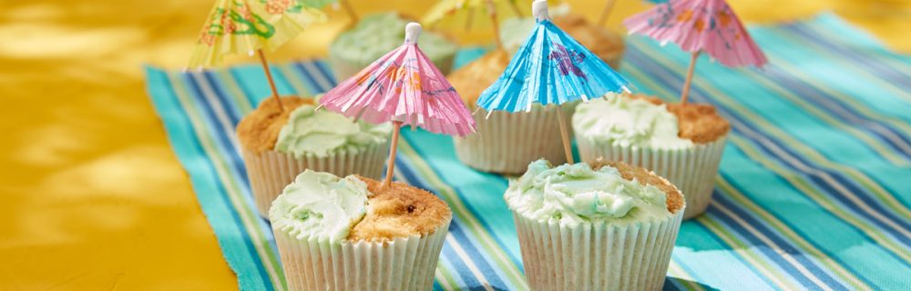 Beach Fun Cupcakes on a beack towel, with paper umbrellas in the top
