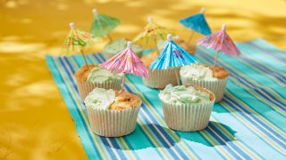 Beach Fun Cupcakes on a beack towel, with paper umbrellas in the top