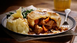 Beef and Ale Pie, served on a white plate with mashed potatoes, green beans and gravy, with a slice missing to show the filling