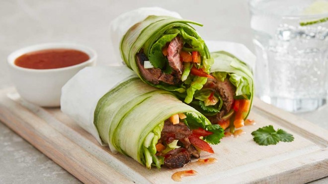 Three Roast Beef Rolls stacked on top of one another on a wooden board, next to a bowl of sweet chilli sauce