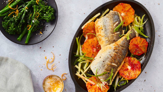 Blood Orange Seared Sea Bass served in a black pan next to a dish of cooked broccoli