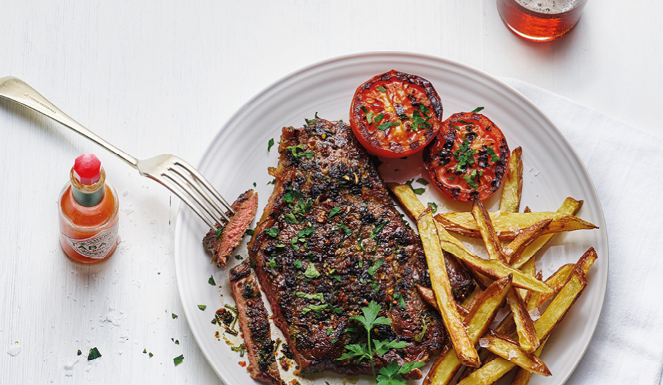 Bloody Mary Rump Steak served on a white plate with homemade chips, grilled tomatoes and topped with parsley