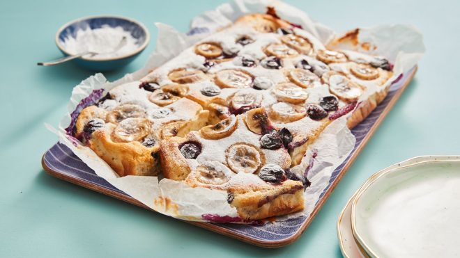 Banana and Blueberry Traybake Pancake served on a blue plate with a slice cut to see the filling