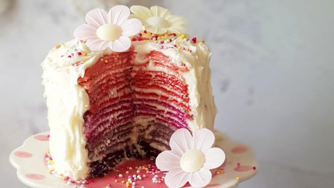 Ombre Crepe Cake toppped with sprinkles and edible flowers, with a portion removed to see the ombre effect inside