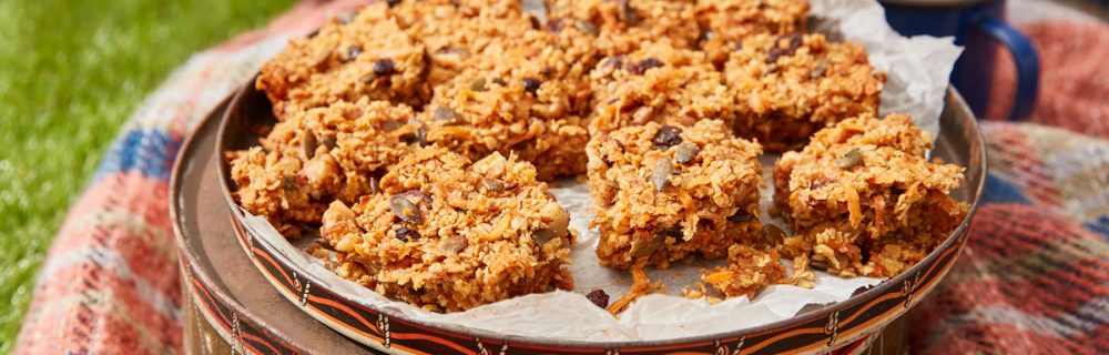 Carrot Cake Flapjack served on top of a cake tin, on a picnic blanket with two cups of tea