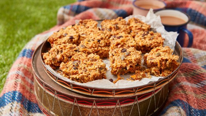 Carrot Cake Flapjack served on top of a cake tin, on a picnic blanket with two cups of tea