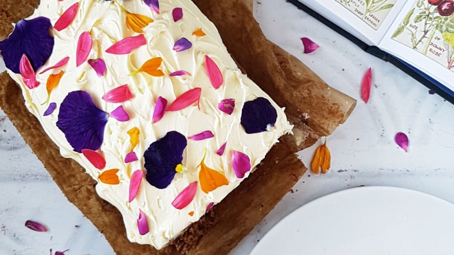 Carrot and Courgette Cake, served on baking parchment and decorated with cream cheese frosting and edible flowers