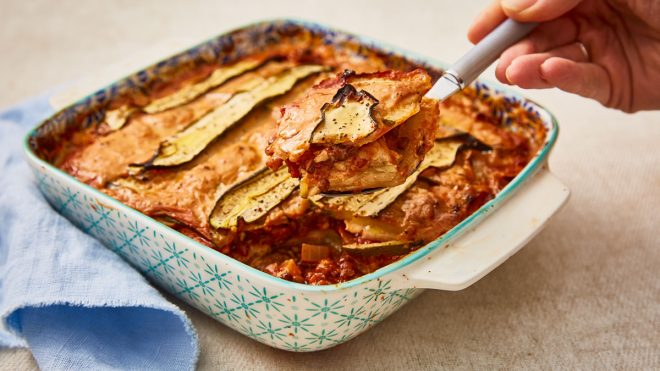Celeriac, Courgette and Puy Lentil Lasagne served in a casserole dish with a portion being lifted out with a spoon