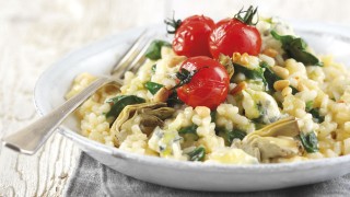 Cheese, Artichoke and Spinach Risotto topped with vine tomatoes and pine nuts served in a white bowl