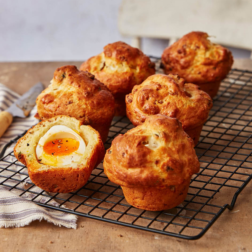Image of cheesy, sausage and egg muffins on a cooling rack with one cut in half