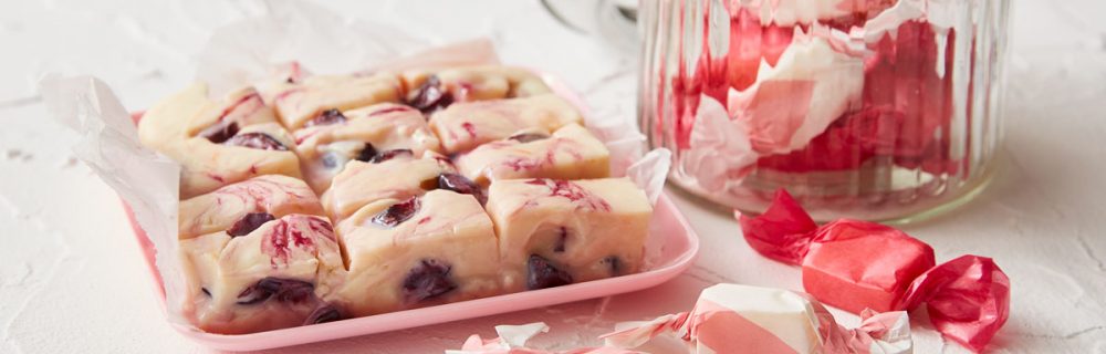 Cherry Ripple Fudge served on parchment paper next to a glass jar of wrapped portions