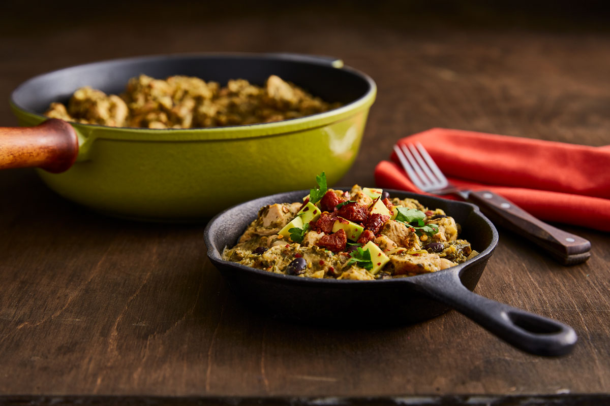 Chicken Chilli with Avocado and Chorizo served in a pan and a small skillet on a wooden table