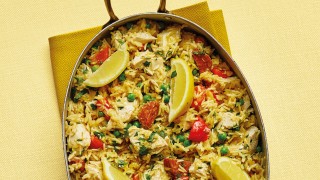 Chicken and chorizo paella served in the pan with lemon wedges on a yellow tablecloth