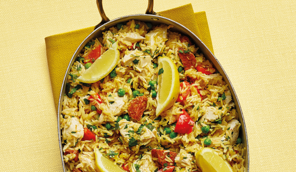 Chicken and chorizo paella served in the pan with lemon wedges on a yellow tablecloth