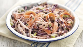 Summer Coleslaw served in a white and blue bowl on top of a striped tablecloth