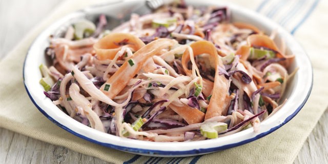 Summer Coleslaw served in a white and blue bowl on top of a striped tablecloth