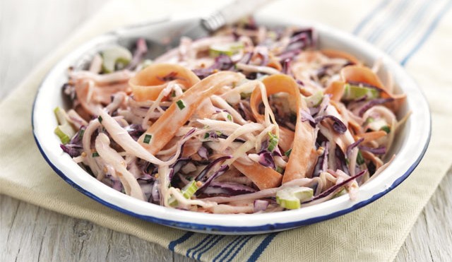 Summer Coleslaw served in a white and blue bowl on top of a striped tablecloth