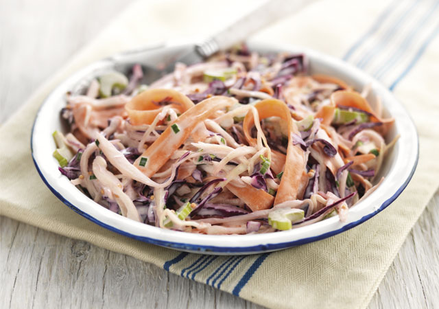 Summer Coleslaw served in a white and blue bowl on top of a striped tablecloth