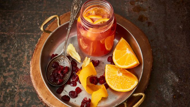 Warm Cranberry and Orange Cider Punch served in a glass jar next to sliced oranges