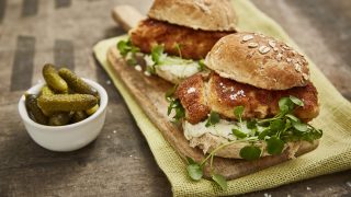 Crispy Fish Burgers served on a wooden board with watercress, next to a bowl of gherkins