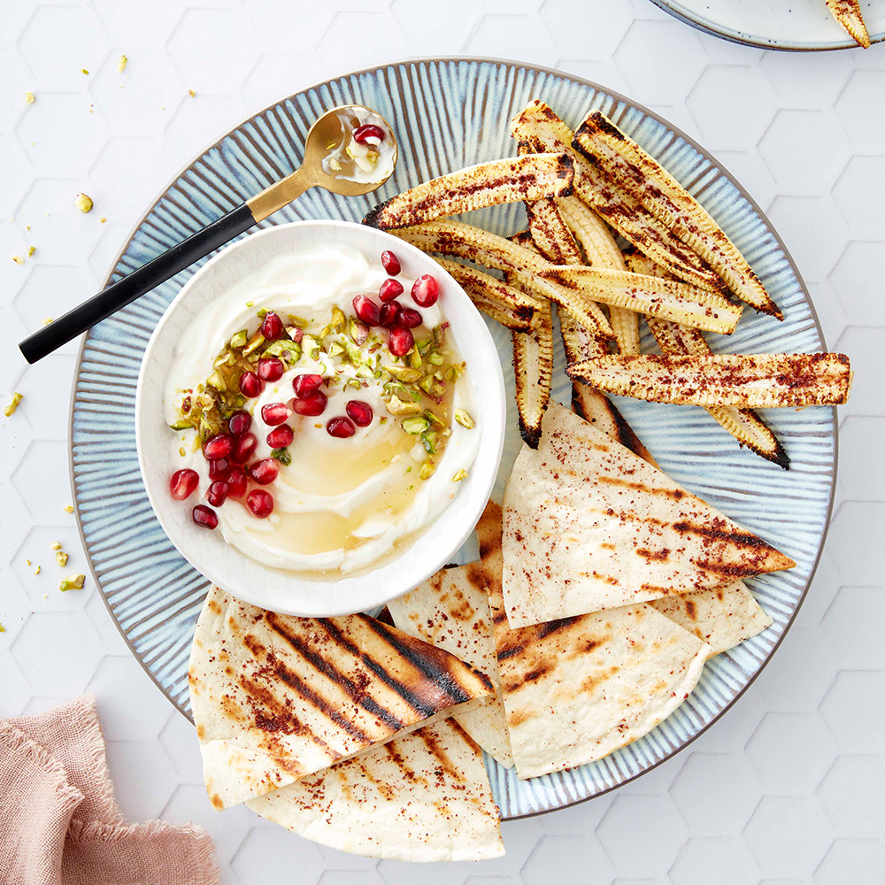 Image of a bowl of whipped goats' cheese dip on a plate with grilled tortilla chips and charred corn