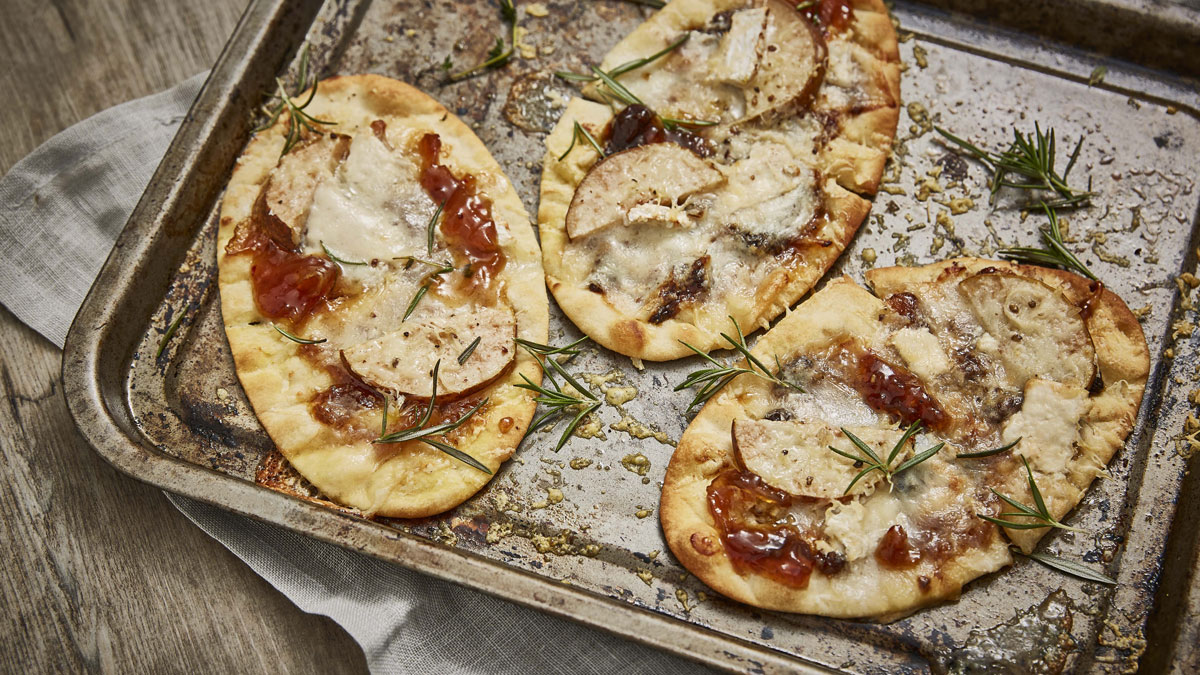 Goats' Cheese, Caramelised Onion and Pear Flatbreads topped with rosemary and served on a baking tray