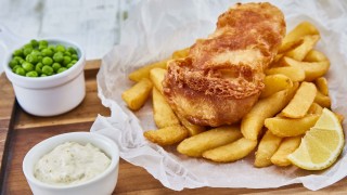 Gluten Free Beer Battered Fish served on top of chips, with a lemon wedge, peas and tartare sauce on baking parchment