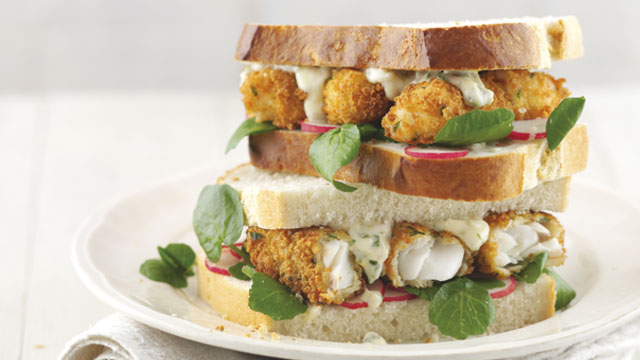The Ultimate Fish Finger Sandwich served on white bread with watercress, with one sandwich half stacked on top of the other