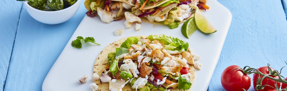 Fish Tacos served on a white board with lemon wedges and coriander