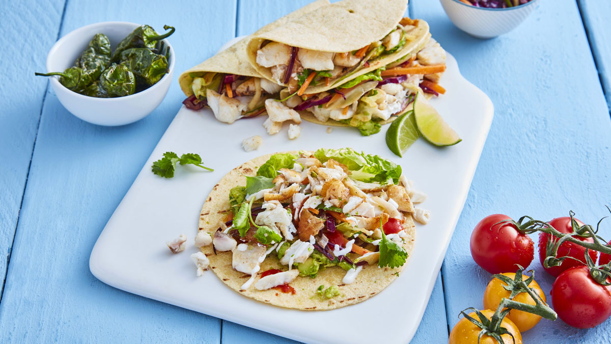 Fish Tacos served on a white board with lemon wedges and coriander