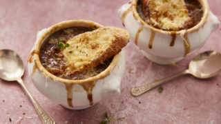 Frech Onion Soup served in white soup bowls with cheese baguettes placed on top