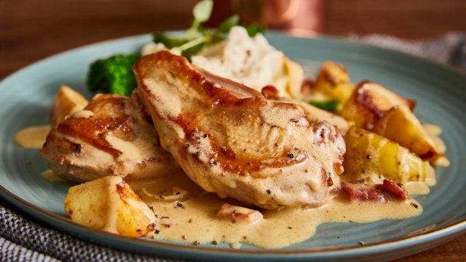 Fricassee of Pheasant, Apples with Cider Crème Sauce served on a blue plate with mashed potatoes and green veg