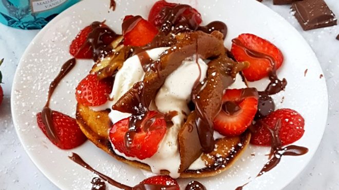 Fully Loaded Griddle Waffles served on a white plate covered in strawberries, vanilla ice cream and chocolate caramel sauce