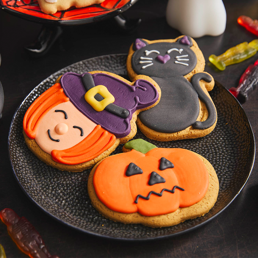 Three biscuits iced to look like a witch, a pumpkin and a black cat laid out on a plate