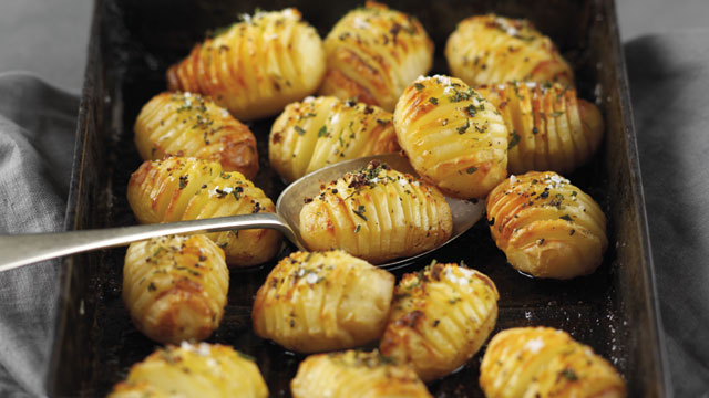 Roasted Hasselback Potatoes served in a metal tray, sprinkled with salt, pepper and rosemary