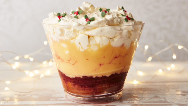 Super Simple TastyTrifle served in a glass bowl, topped with sweet holly leaves with lights in the background