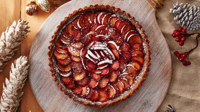 Spiced Plum Tart with Gingerbread Crust served on a wooden board and dusted with icing sugar