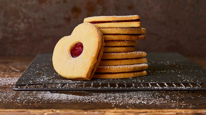 Jammy Love Heart Sandwich Biscuits stacked on top of each other and served on a cooling rack