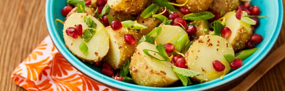 Jewelled Potato Salad served in a blue bowl with a wooden spoon