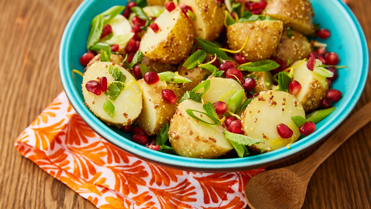 Jewelled Potato Salad served in a blue bowl with a wooden spoon