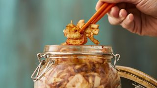 Kimchi being served from a glass jar with chopsticks