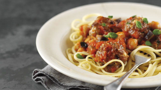 Greek Lamb Meatballs served on top of linguine in a white bowl with a fork