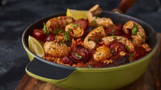 Sausage, Chorizo and Langoustine Jambalaya served in a gree skillet on top of a wooden board