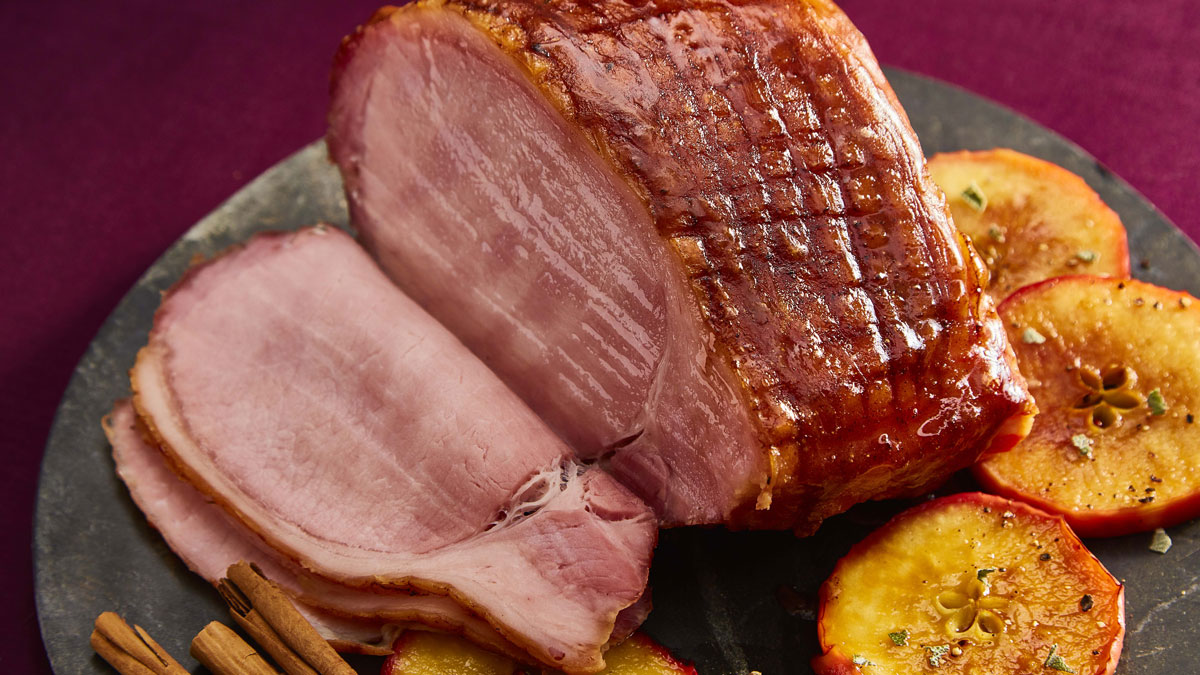 Festive Maple Syrup Spiced Ham served on a marble plate and sliced served with baked apples
