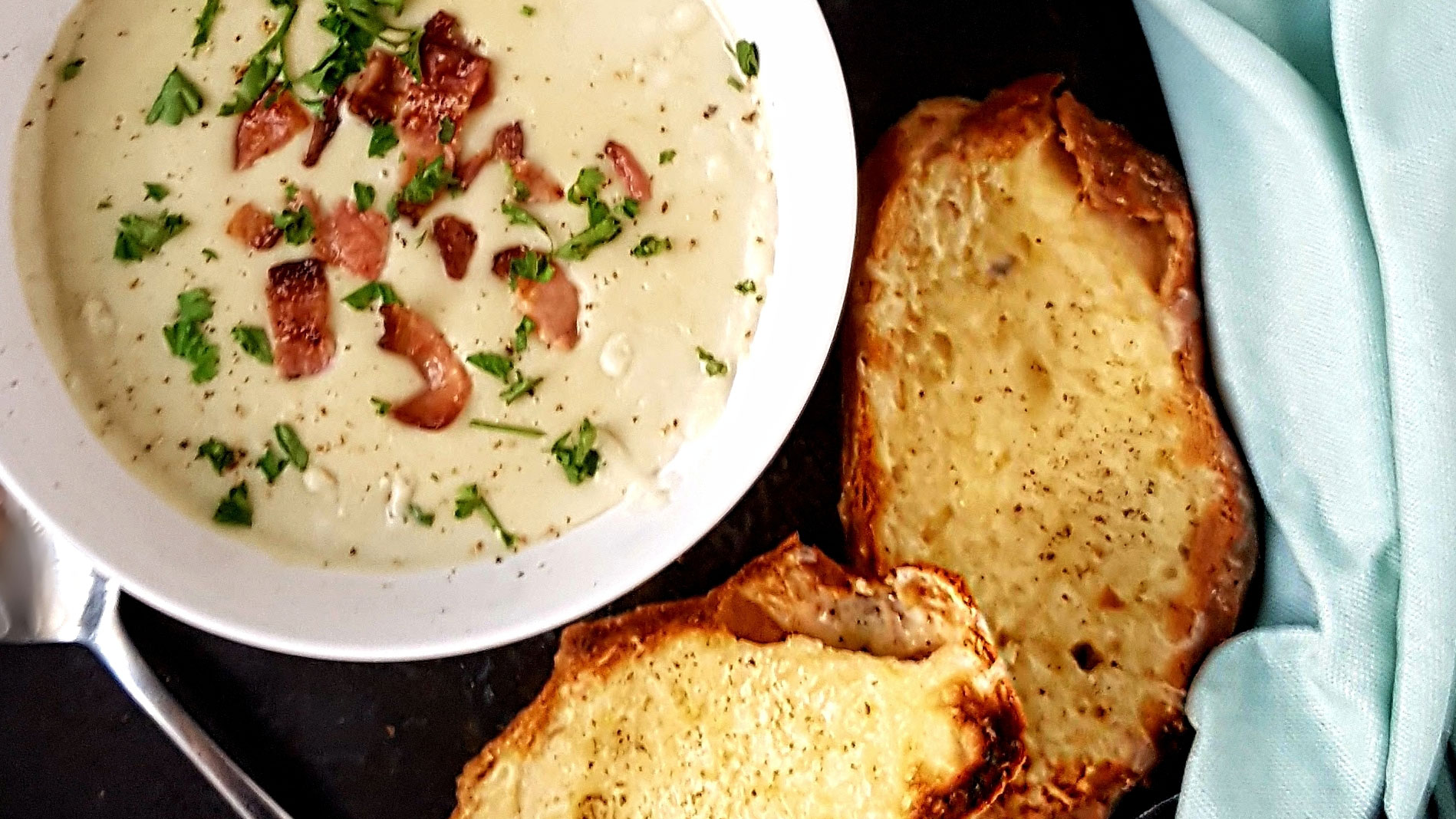 Stilton and Bacon Soup with Cheese and Garlic Slices served in a white bowl next to a blue tablecloth