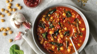 Moroccan Chickpea and Lentil soup served in a dish on top of a grey cloth. Next to a raw garlic bulb and chickpeas